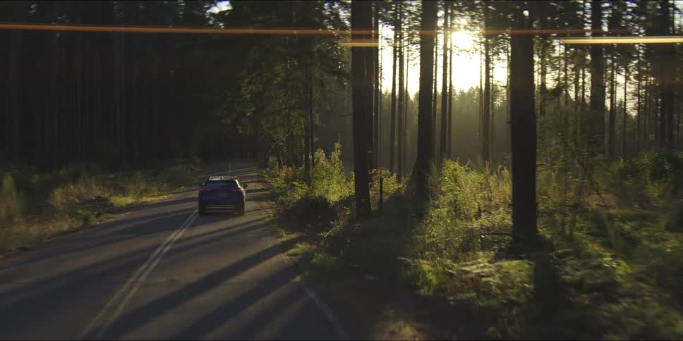 Blue personal car driving on a road surrounded by trees outdoors during day time