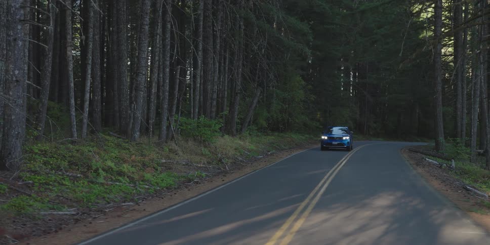 A blue car drives on a remote road in an evergreen forest