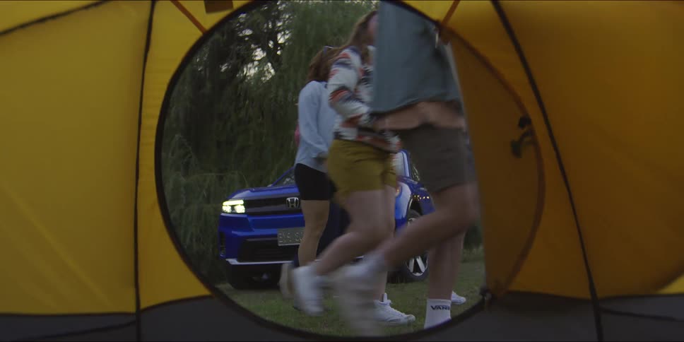 Mirror in a tent reflects people walking past a car with its headlights on in the early evening