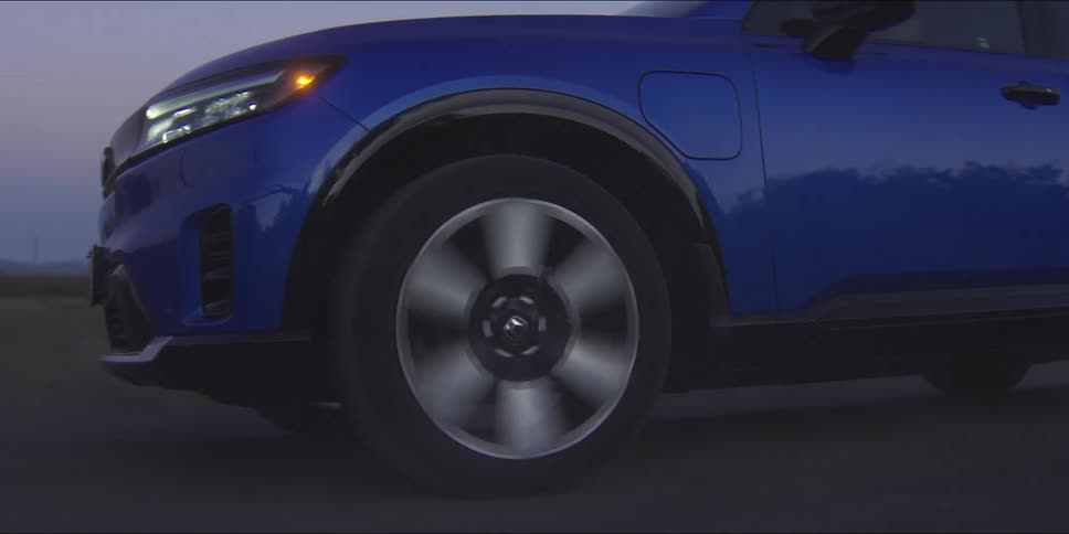 A blue suv speeds along at dusk its spinning wheel blurred with motion as the road fades into the evening light