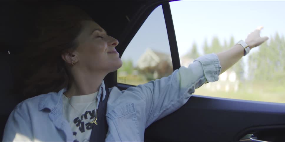 Woman sitting in the back seat of a traveling automobile with her arm out of the open window