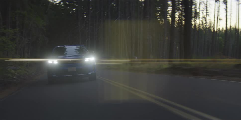 A blue suv glides along a quiet forest road motionblurred against tall trees and soft green undergrowth filtering the sunlight