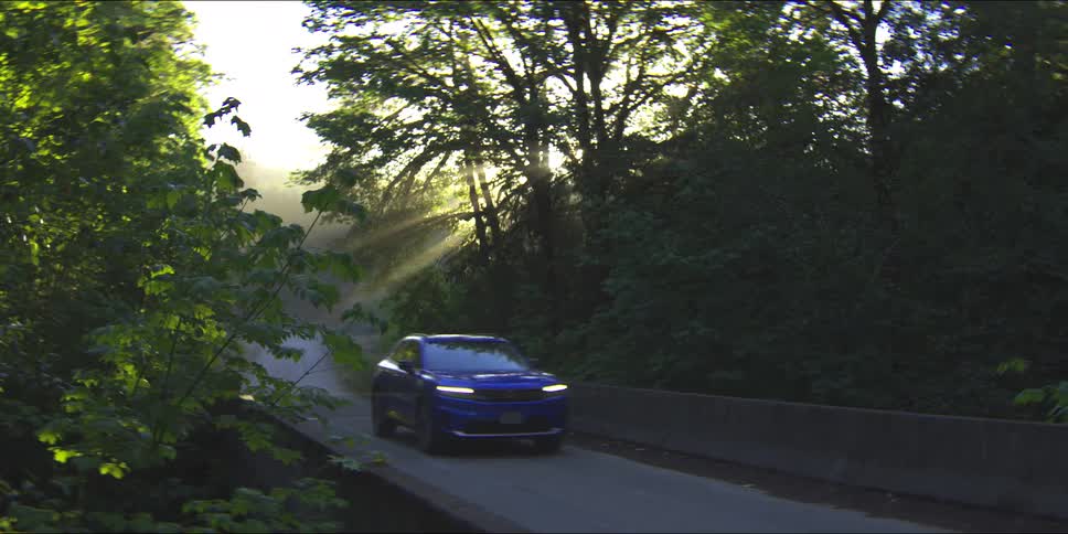 Car travels on a road through a forested mountain as sunlight shines through the trees