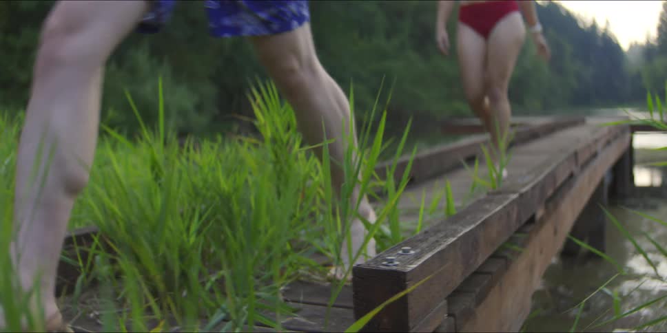 Three people in swimsuits walk back from a wooden dock on a lake