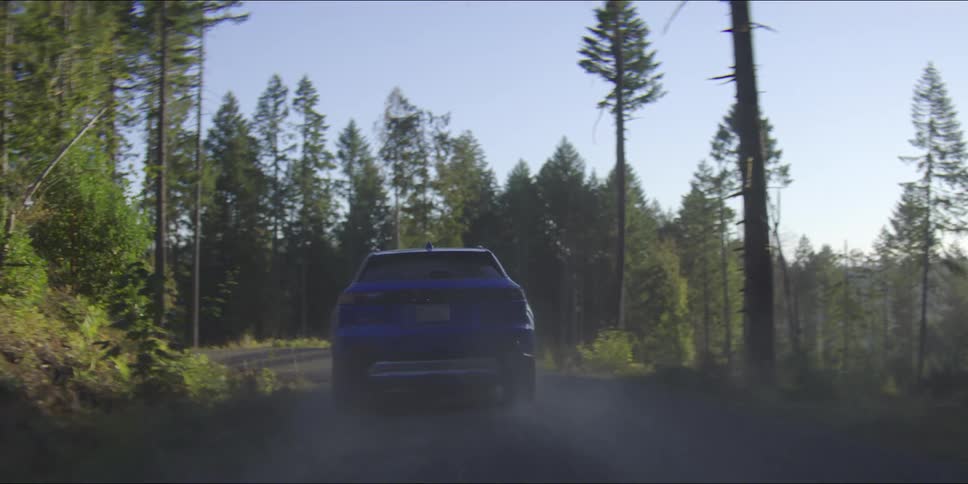 Car traveling on a forested mountain road leaving behind a trail of dust and smoke