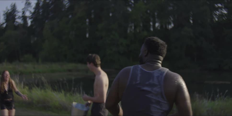 Two men and one woman are on a dirt road near a lake in a play water fight with buckets of water