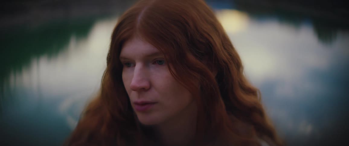 Redheaded woman standing near the water looks around
