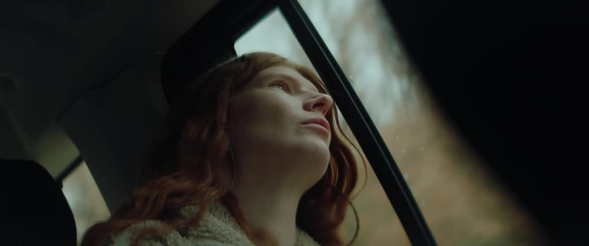 Young adult woman sitting inside of a car and looking out of the window with a contemplative face expression during day time