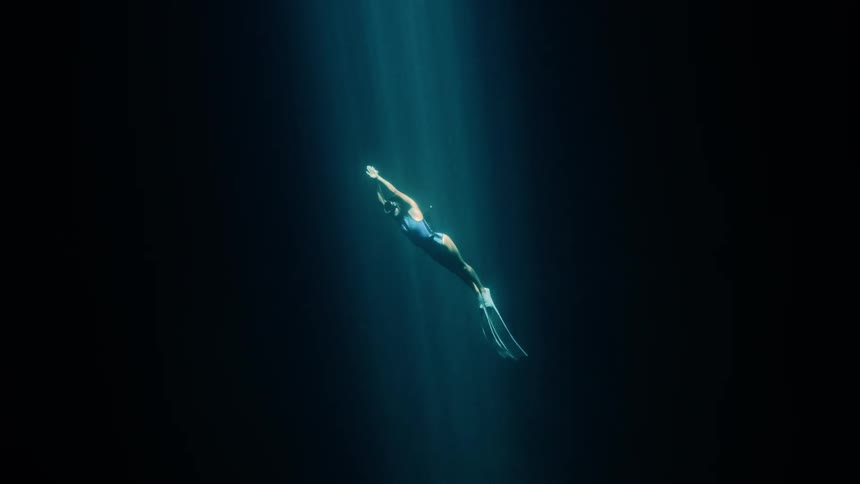 Adult woman wearing swimming goggles and fins diving underwater