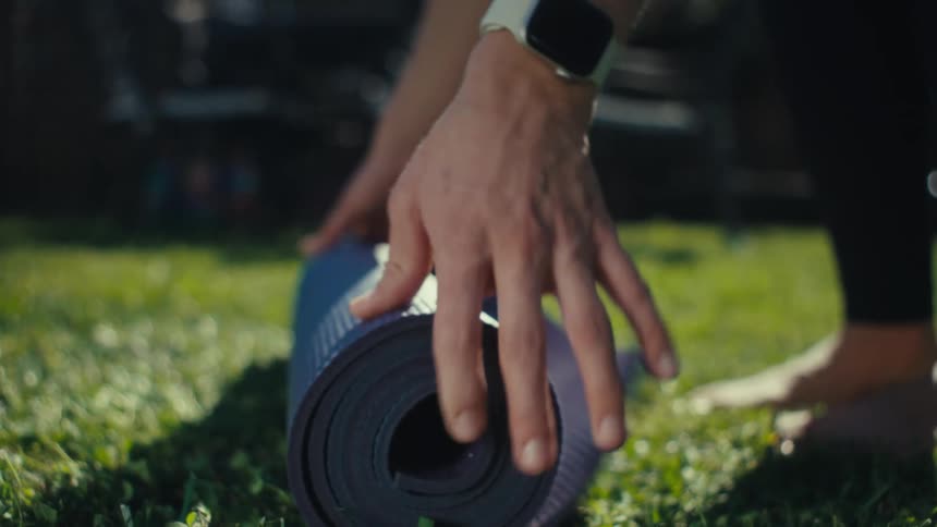 Woman places a rolled up mat on the grass in her yard and pushes it so it unrolls