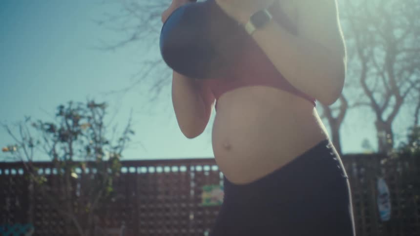 Expectant mother exercises with a weight outdoors on a sunny day