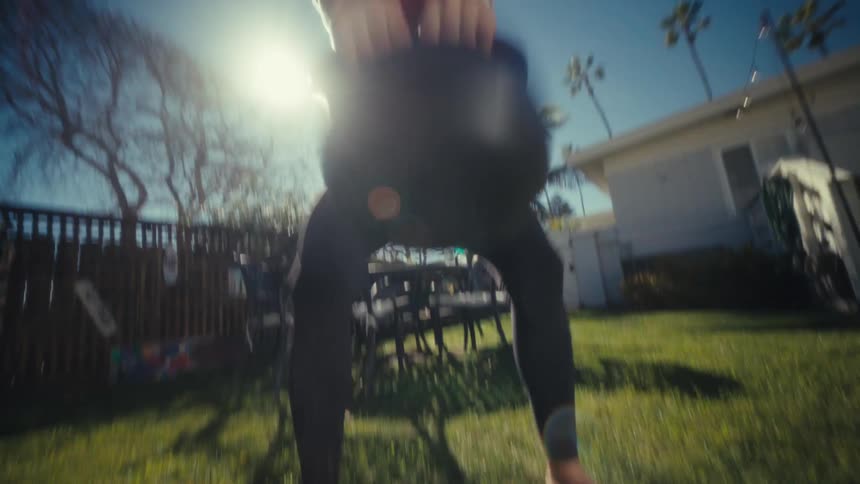 The woman is lifting a kettle bell in the yard