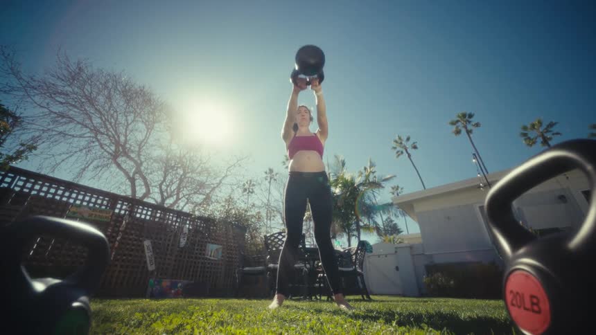 Expectant mother exercises with a weight while standing in her backyard on a sunny day
