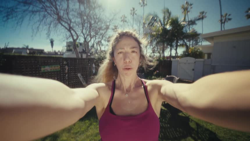 A woman in a sunny backyard is shown close up from the waist up moving up and down