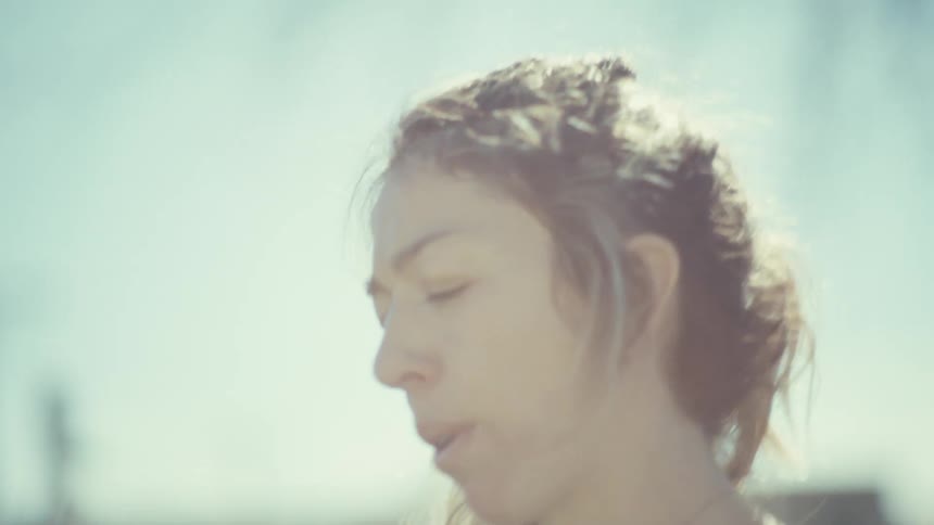 A pregnant woman wearing a purple sports bra and black leggings stands barefoot on green grass while breathing deeply and looking down during a bright day