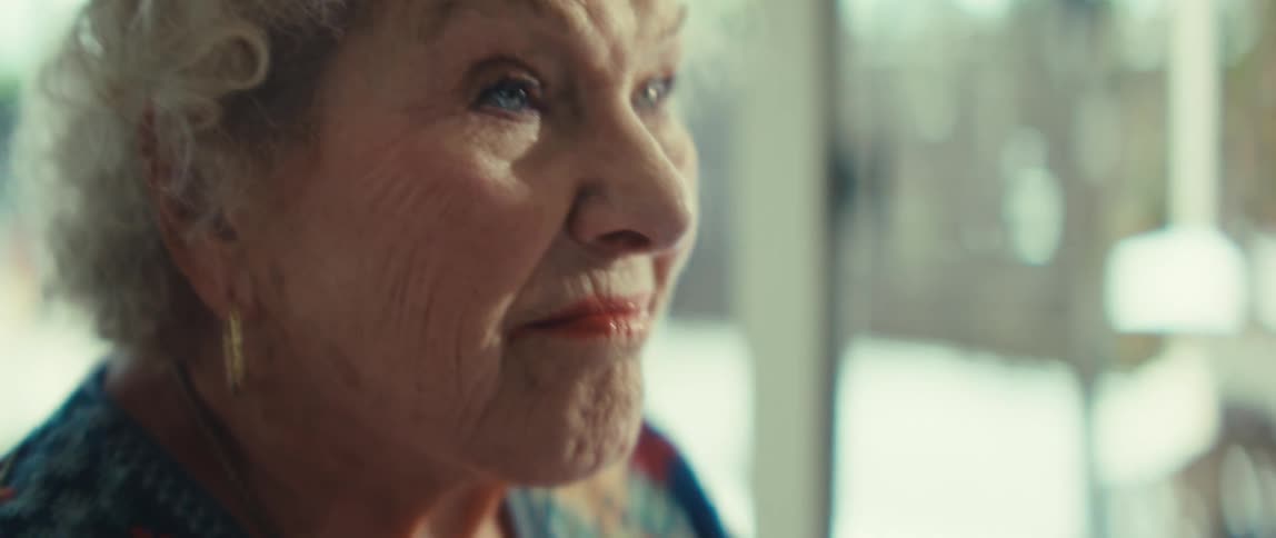 An elderly woman with curly white hair looks thoughtfully into the distance while holding a document filled with bar charts
