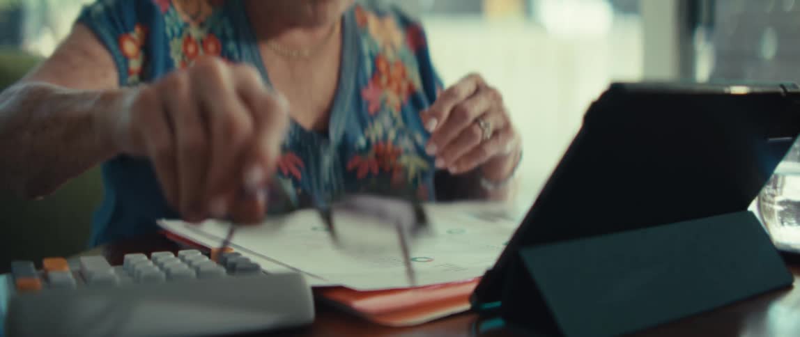 An elderly woman takes off her glasses before tapping on her tablet computer