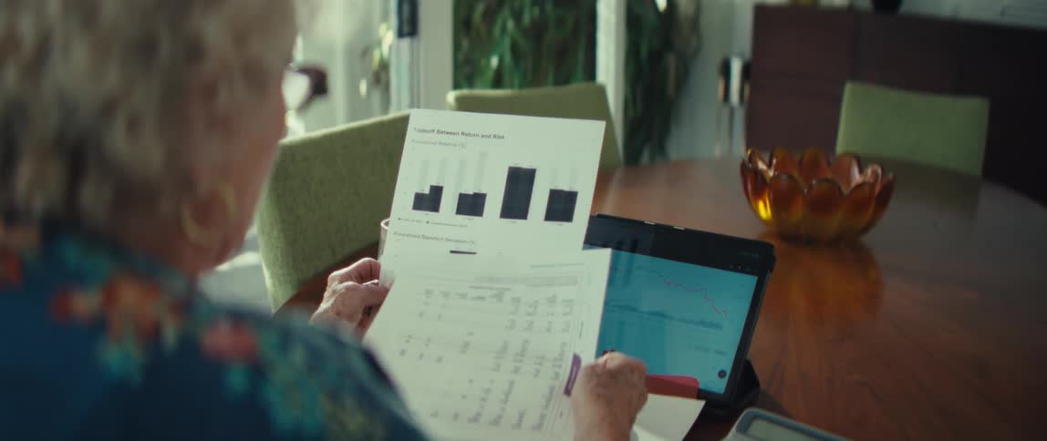 Woman sits at a table with a tablet computer reading financial paperwork