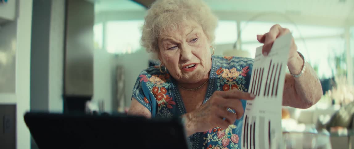 Woman sits at a table with a tablet computer holding up a document pointing and explaining the graphs