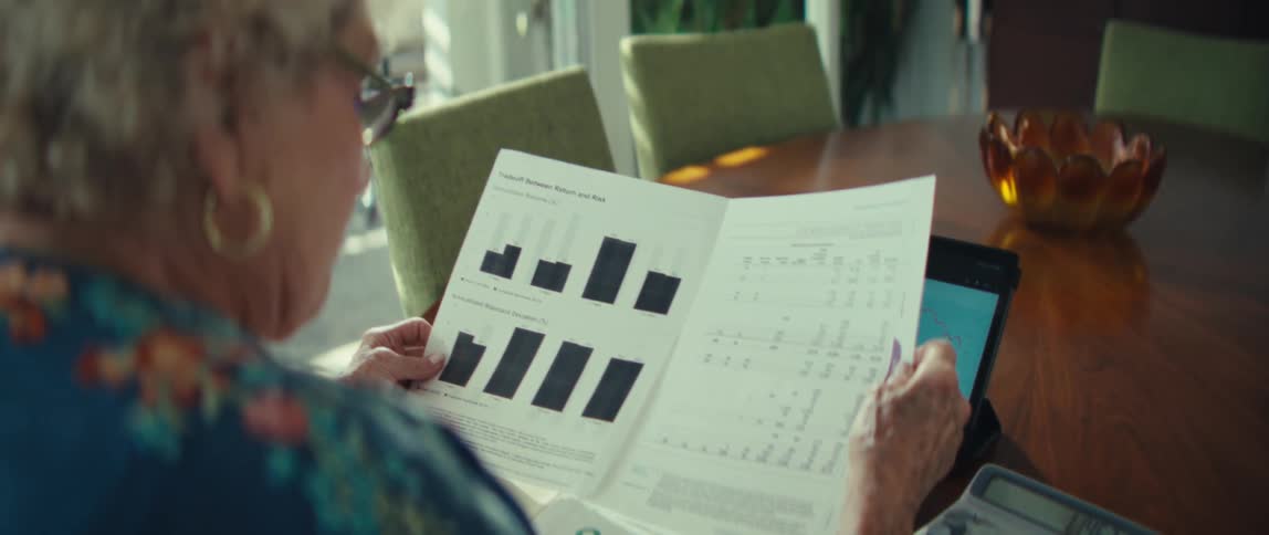 An elderly woman looks at some documents with her tablet nearby