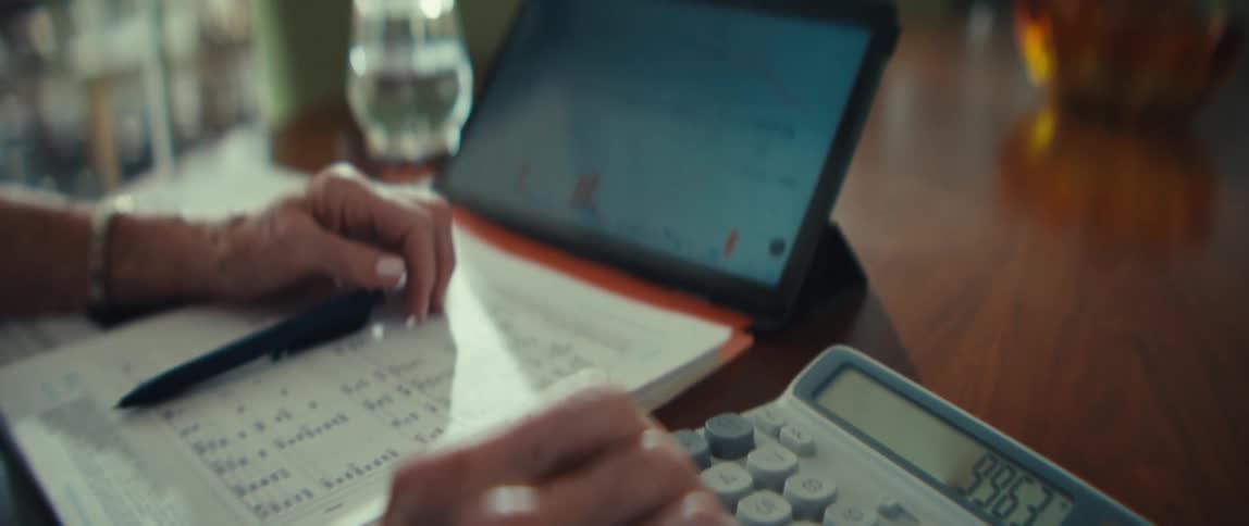 Woman sits at a table with a tablet computer figuring financial paperwork with a calculator