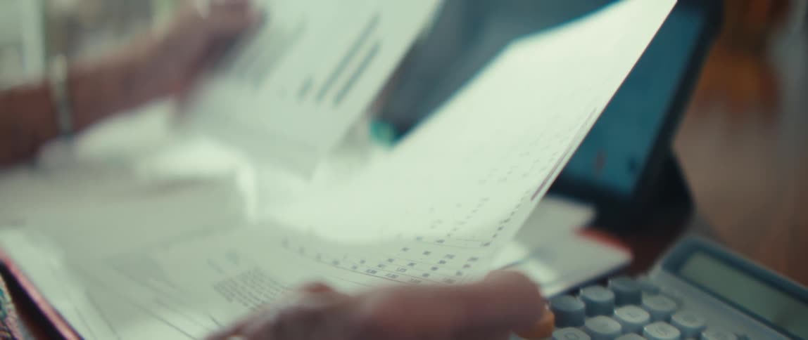 Woman sitting at a table with a tablet computer and a calculator as she reads documents