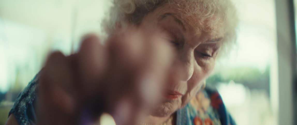 Elderly woman sitting at home consults a document and uses a large calculator
