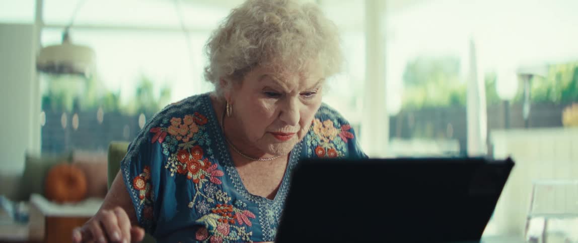 Elderly woman uses a calculator while referencing a tablet while at home during the daytime
