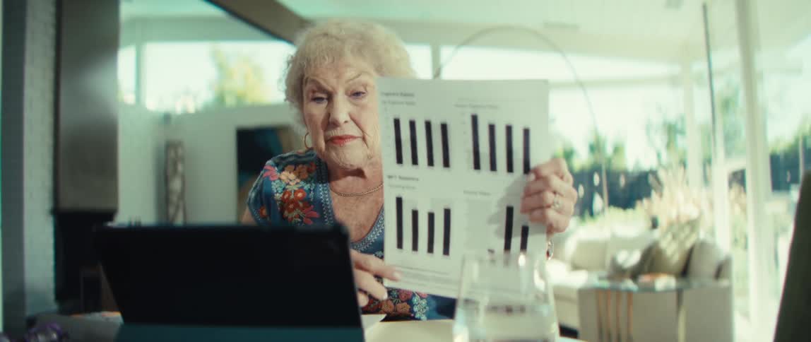 The woman is using a tablet and pointing to a chart on the papers