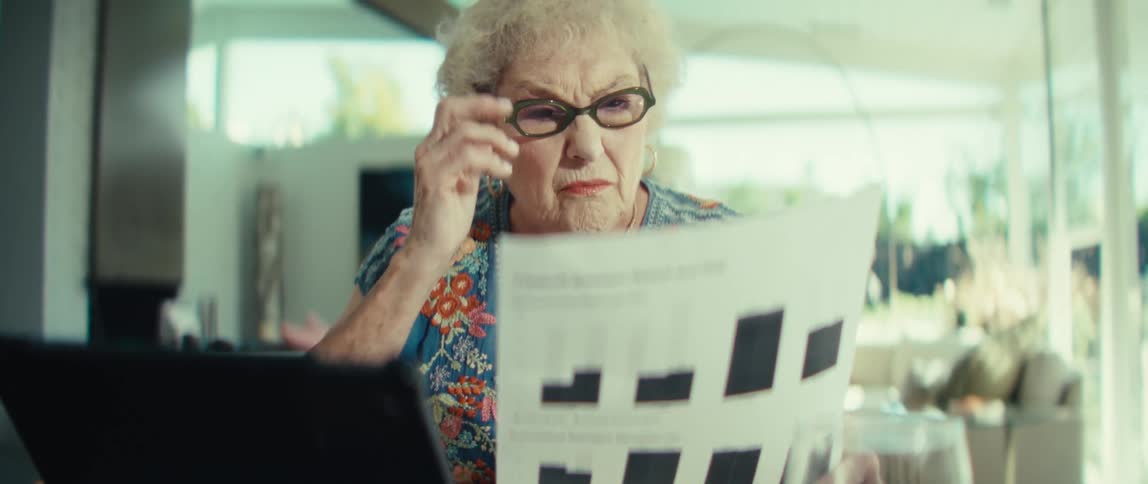 An elderly woman puts on her glasses and reviews some documents