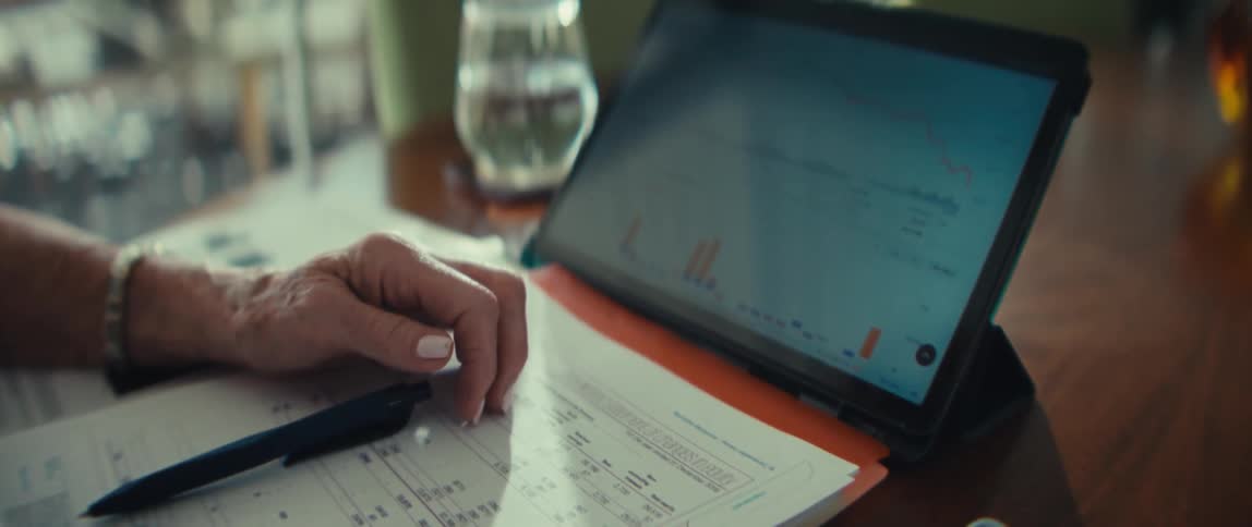 Woman sits at a table with a tablet computer figuring financial paperwork with a calculator