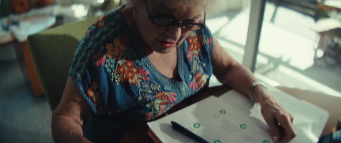 An elderly woman wearing glasses uses a calculator while sitting down
