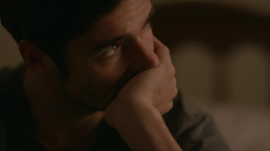 A seated man stares in deep thought while inside a residence