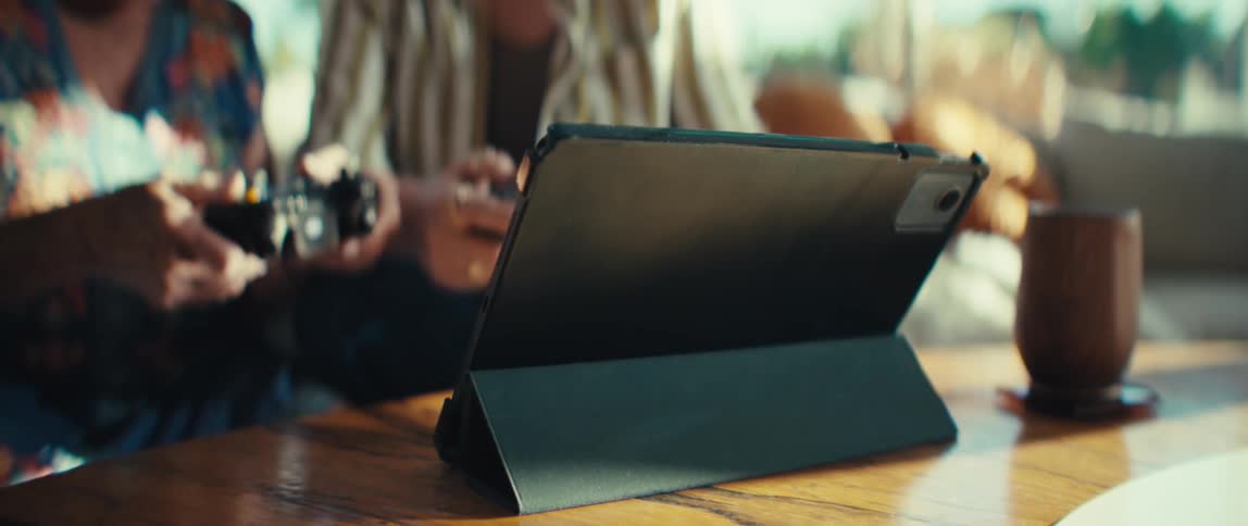Two women sitting on a couch playing video games on a tablet computer as they move the controllers in excitement