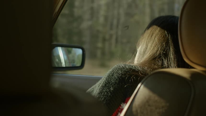 A woman points out the window in a moving car