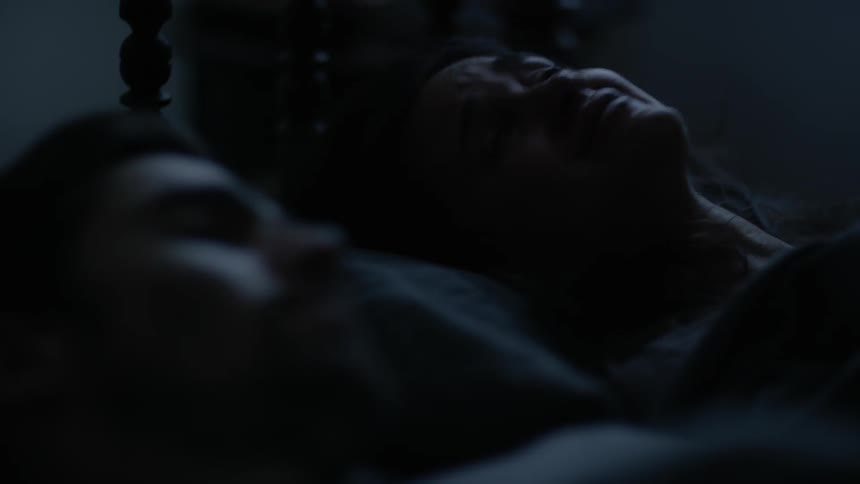 Woman lays crying in bed next to sleeping man