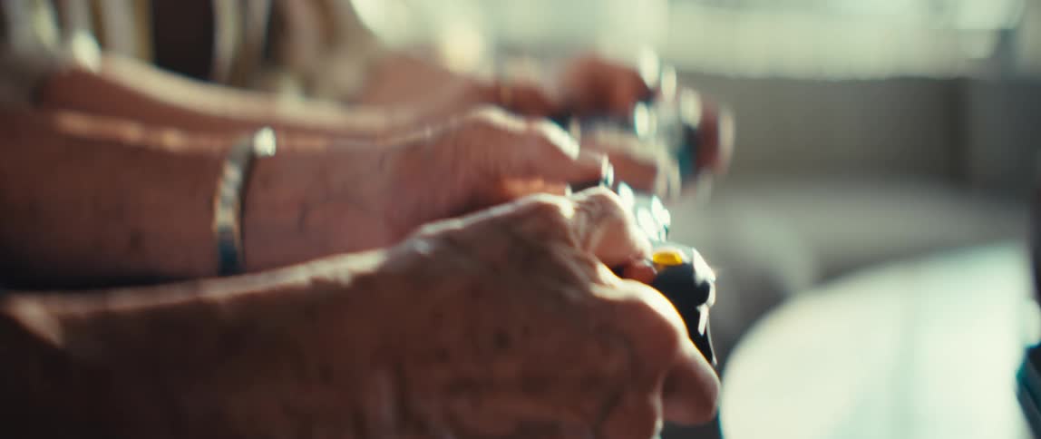Two people are sitting sidebyside holding video game controllers the camera focuses on their hands as they press buttons and move the joysticks