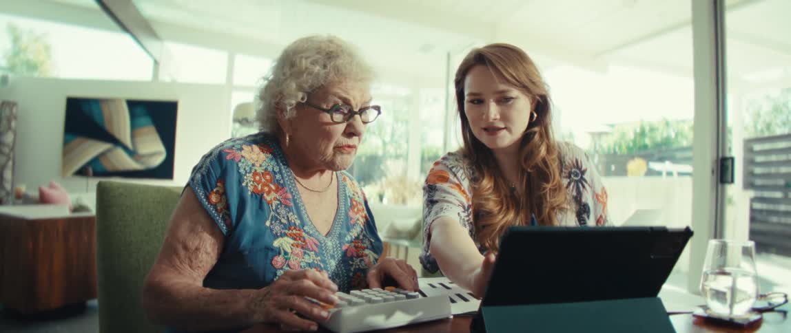 Two women sitting at a dining table using a tablet and calculator in a bright modern home