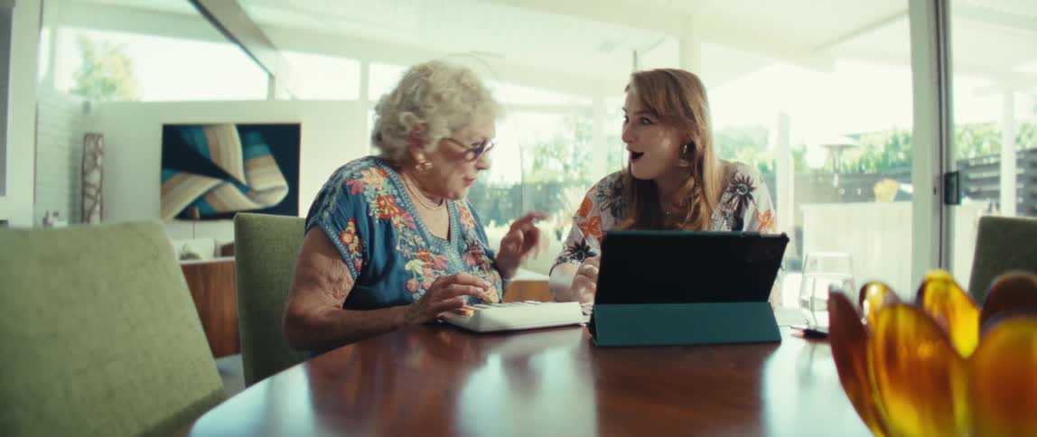 Two women sitting at a table with a tablet computer and paperwork as they talk