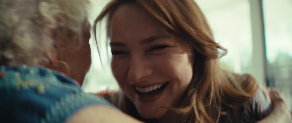 Two women sitting side by side on a couch in the living room hugging each other excitedly