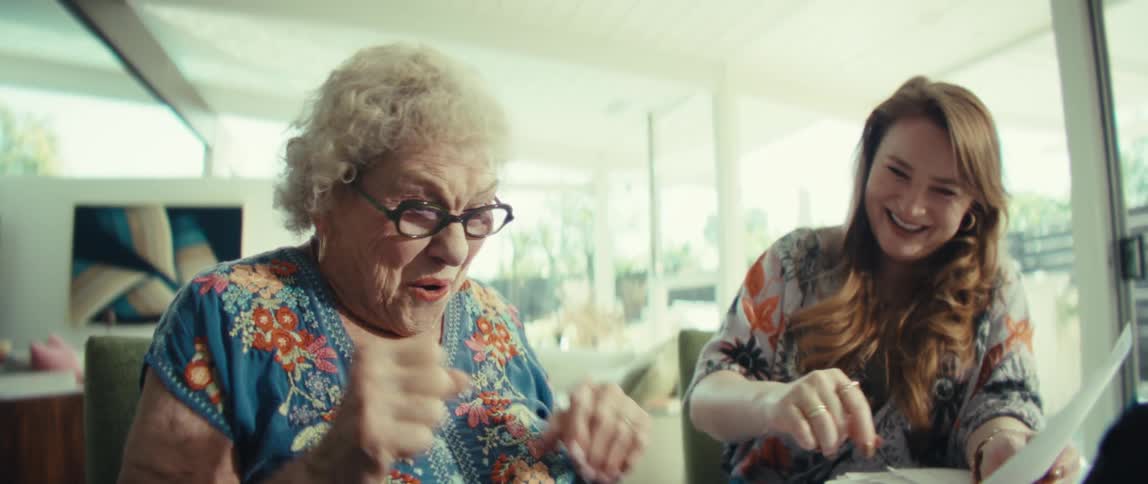 Two women looking at a screen with the young woman explaining something to the elderly woman both become excited highfive and smile in the living room at midday