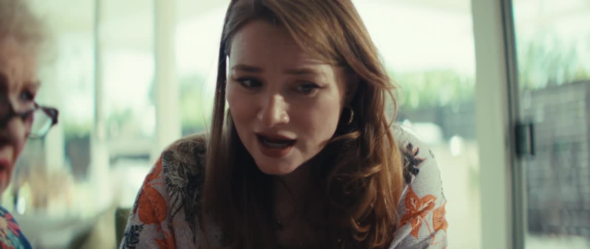 A younger woman who is sad talks to an elderly woman at a desk in a room