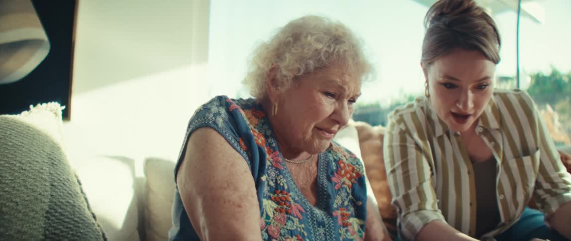 Elderly woman and her daughter play video games in the living room during the day