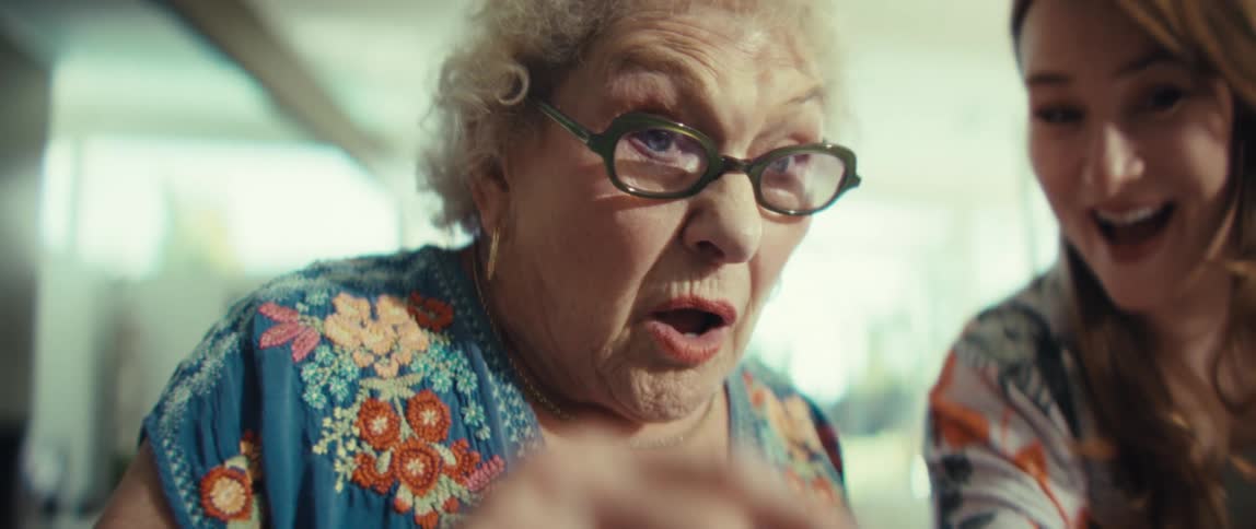 An elderly woman and a younger woman share a moment of shocked amazement and joyful laughter while looking at a tablet together