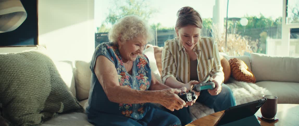 A young woman teaches an elderly woman how to play video games on a tablet