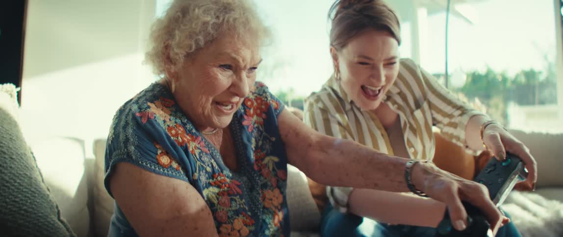 An elderly woman and a younger woman cheer with excitement while playing video games together