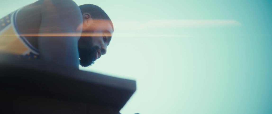 A man with a beard is shown from a low angle as he leans over a wooden railing outdoors he is looking down at a smartphone held in his hands against a bright clear sky