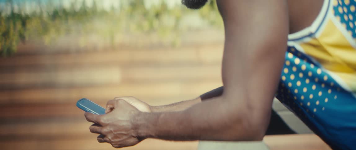 A male athlete resting on a platform on the field at midday smiling while texting