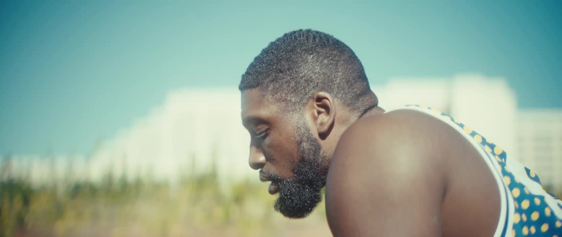 A focused athlete in a tank top rests outdoors while looking at his smartphone