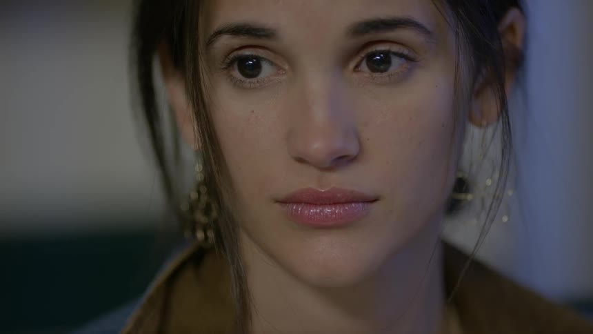 A woman with flower earrings blinks and looks toward someone